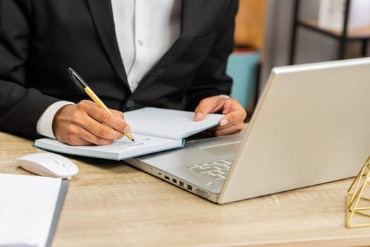 Close-up hands of focused businessman freelancer working at modern home office workplace desk writing notes ideas in notebook. Male in formal suit preparing planning presentation startup project