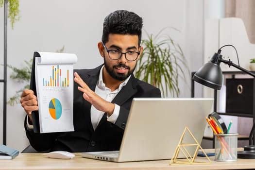 Indian businessman freelancer making online presentation video laptop call education lessons for remote study student classes at office workplace. Male Arabian in suit demonstrates graphic analytics