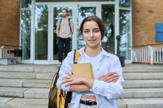 Portrait of high school student, smiling girl with backpack looking at camera, outdoor on steps of educational building. Adolescence, 15, 16, 17 years old, lifestyle, education concept