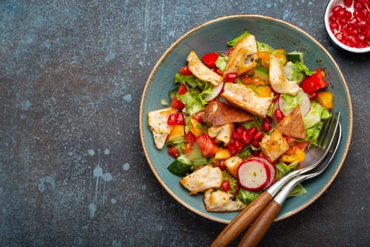 Traditional Levant dish Fattoush salad, Arab cuisine, with pita bread croutons, vegetables, herbs. Healthy Middle Eastern vegetarian salad on plate, rustic dark blue background top view, copy space.