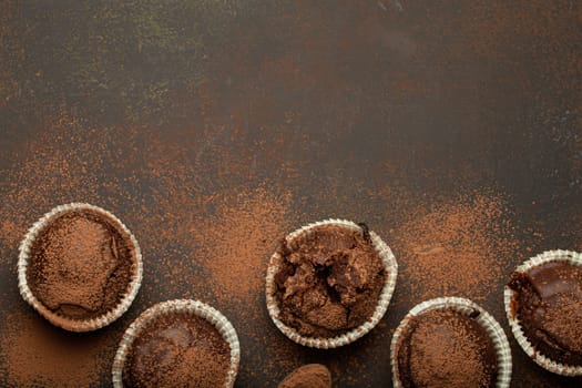 Chocolate browny muffins and cocoa in teaspoon top view on brown rustic stone background, sweet homemade dark chocolate cupcakes.