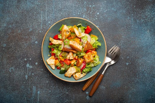 Traditional Levant dish Fattoush salad, Arab cuisine, made with pita bread croutons, vegetables and herbs. Healthy Middle Eastern vegetarian salad on plate, rustic dark blue background top view.