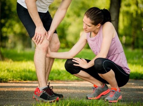 Woman helps to man with injured knee at sport activity