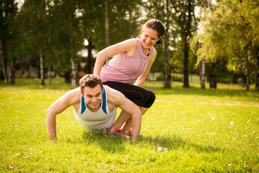 Sport man making push-ups while woman is sitting on him as a weight