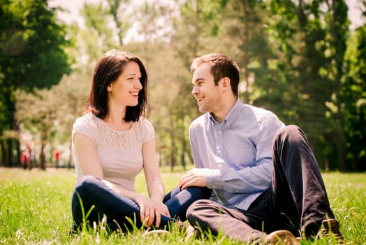 Young happy couple talking together outdoor - sitting on grass in nature