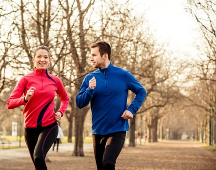 Young couple jogging together in tree alley - late autumn
