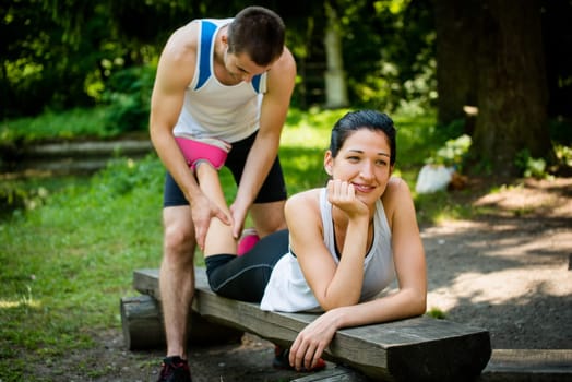 Man gives massage of calf to his girlfriend after sport training - woman lies on bench