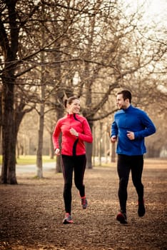 Young couple jogging together in tree alley - looking on each other