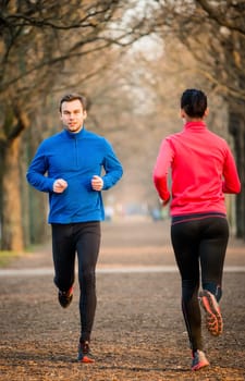 Young man jogging in park, woman running in opposite direction