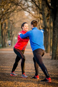 Young couple warming up muscles before jogging - fall nature