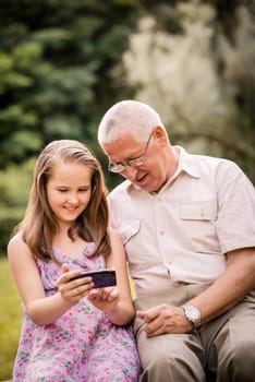 Senior man with his grandchild looking together on photos in smartphone - outdoor in nature