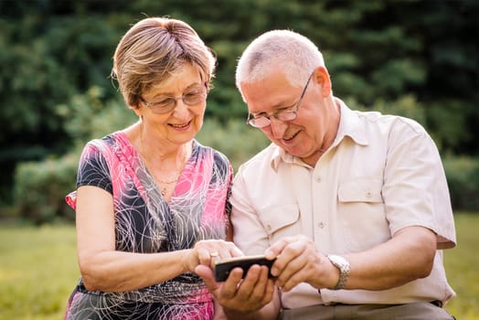 Senior couple looking together on photos in smartphone - outdoor in nature