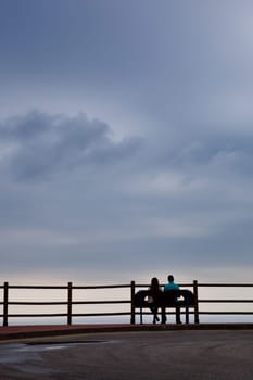Silhouette of a heterosexual young couple on a calm and peaceful cloudy day, relaxing in front of the ocean view