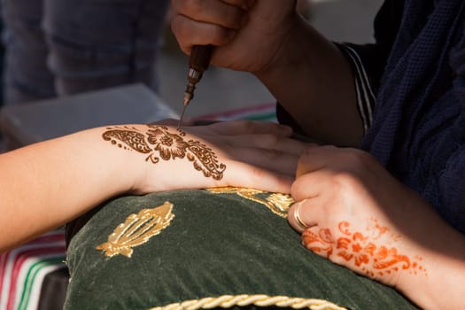 Image detail of henna being applied to hand over green and gold fabric cushion