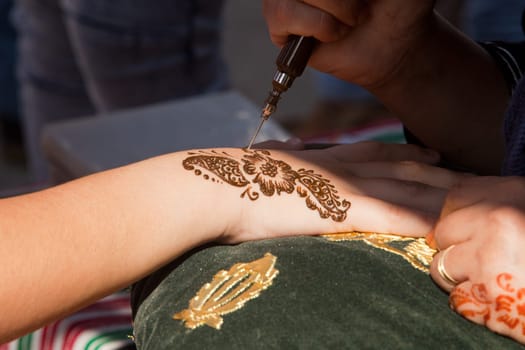Image detail of henna being applied to hand over green and gold fabric cushion