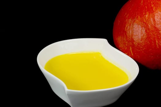 White bowl of pumpkin soup with cream. Red pumpkin is in the background. All isolated on black background.