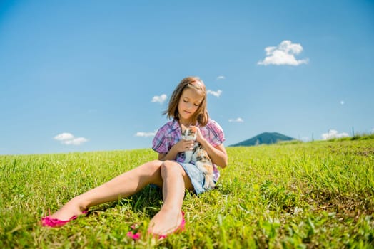Girl sitting in grass and playing with her cute kitten
