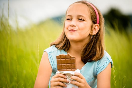 Child eating and relishing chocolate - outdoor in nature