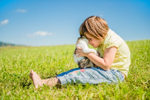 Child sitting in grass and playing with her cute kitten