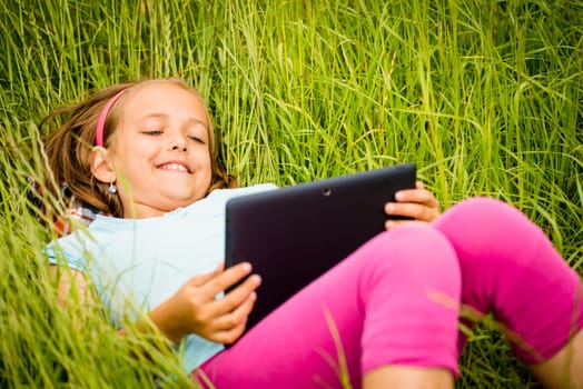 Smiling teen girl lying in grass and watching tablet
