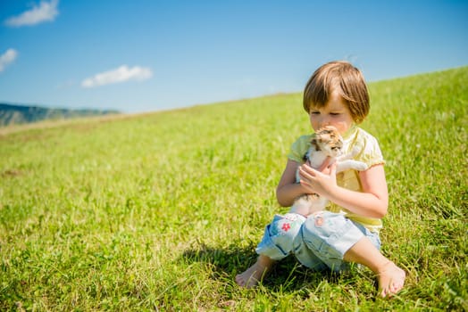 Child sitting in grass and playing with her cute kitten