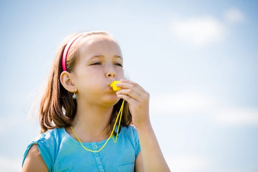 Beautiful child blowing in whistle - outdoor with blue sky