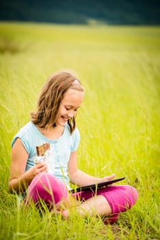 Child eating and relishing chocolate while watching tablet - outdoor in nature