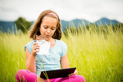 Child eating and relishing chocolate while watching tablet - outdoor in nature