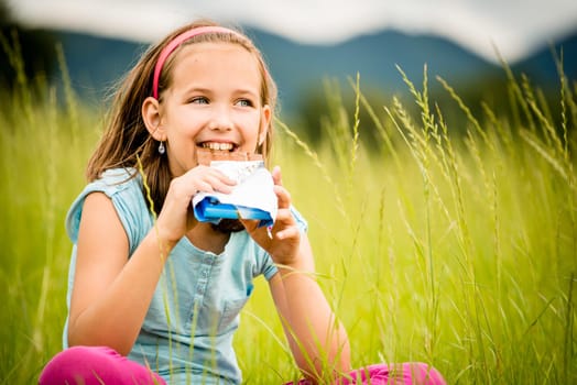 Smiling child eating and relishing chocolate - outdoor in nature