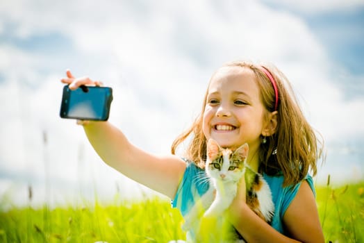 Child taking photo with mobile phone camera of herself and her cat - outdoor in nature