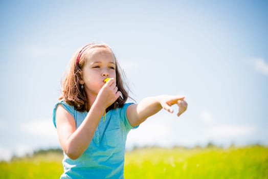 Cute teen girl blowing in whistle and pointing with hand - outdoor in nature