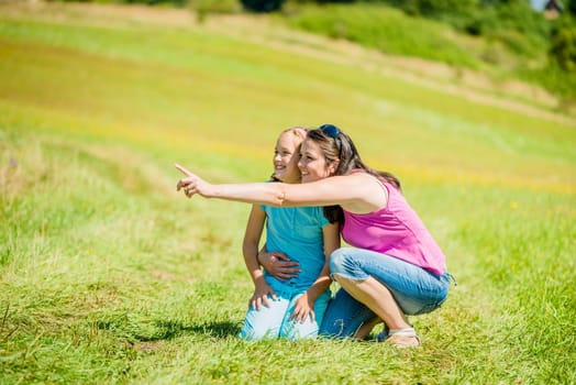 Mother is showing something in distance to her child in nature on sunny summer day