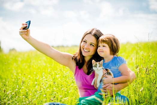 Mother taking photo with her smart-phone camera of herself, her girl and kitten - outdoor in nature