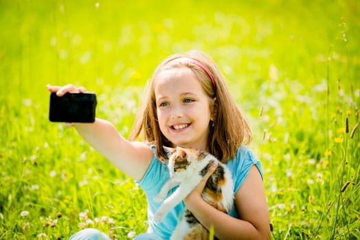 Child taking photo with mobile phone camera of herself and her cat - outdoor in nature