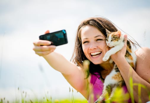 Woman taking photo with mobile phone camera of herself and her cat - outdoor in nature
