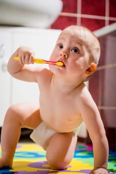 Cute baby cleaning her teeth sitting on floor in bathroom