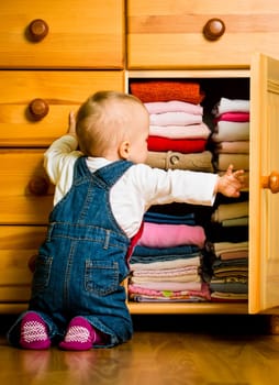 Baby throws out clothes from wooden furniture at home