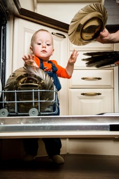 Cute baby helping mother unload dishwasher in kitchen