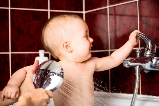 Cute baby playing with water tap in bathroom while at shower