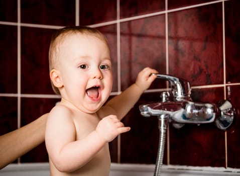 Cute baby playing with water tap in bathroom