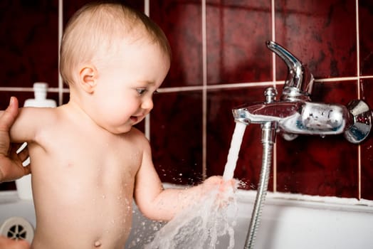 Cute baby playing with water tap in bathroom