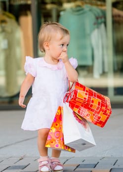 Cute baby goes shopping with bags, shops in background