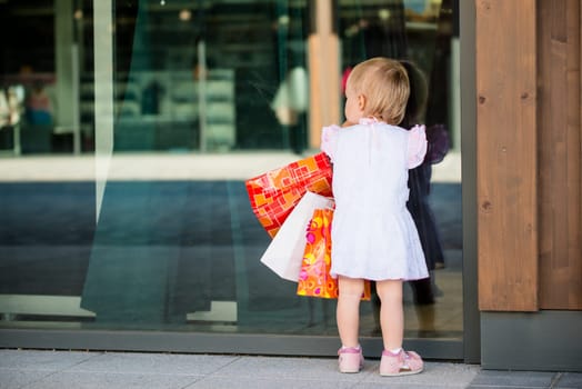 Little girl in white dress looking through shop window