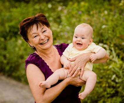 Grandmother with grandchild - senior woman holding her granddaughter outdoor in nature