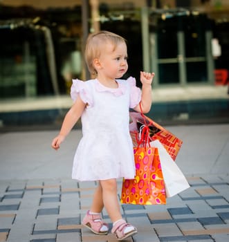 Cute baby goes shopping with bags, shops in background