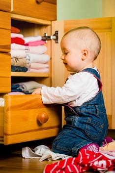 Baby throws out clothes from wooden furniture at home