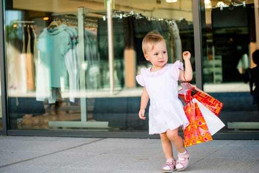 Cute baby goes shopping with bags, shops in background