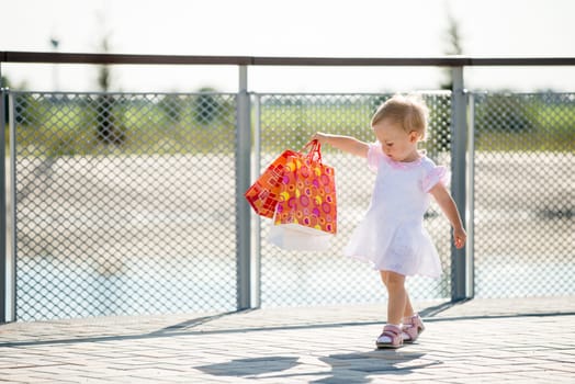 Cute baby goes shopping with bags, outdoor on sunny day