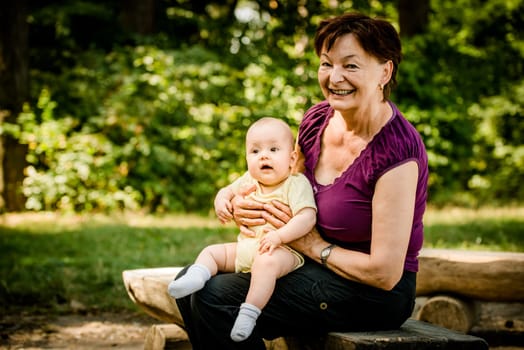 Grandmother with grandchild - senior woman sitting with her granddaughter on bench outdoor in nature