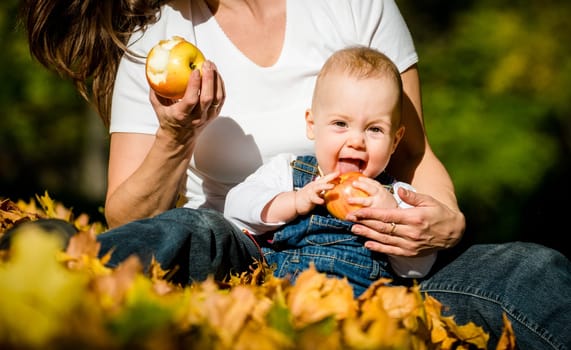 Mother with her cute baby eating apples outdoor in autumn nature